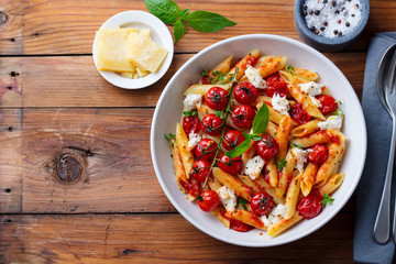 Pasta penne with roasted tomato, sauce, mozzarella cheese. Wooden background. Top view. Copy space.