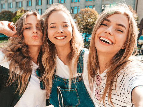 Three young smiling hipster women in summer clothes.Girls taking selfie self portrait photos on smartphone.Models posing in the street.Female showing positive face emotions