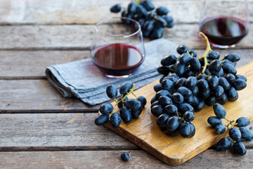 Glass of red wine with fresh grape on wooden table. Outdoor background.