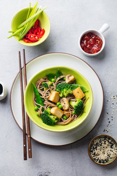 Soba noodles with vegetables and fried tofu in a bowl. Grey background. Top view.