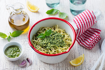 Pasta spaghetti with basil pesto sauce in saucepan. White wooden background.