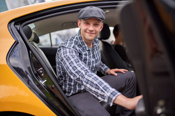 Image of happy man in cap and plaid shirt looking to camera sitting in back seat in yellow taxi