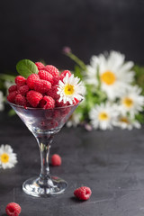 Fresh Deluxe Raspberries in martini glass with field flowers on dark wooden background, vertical composition.