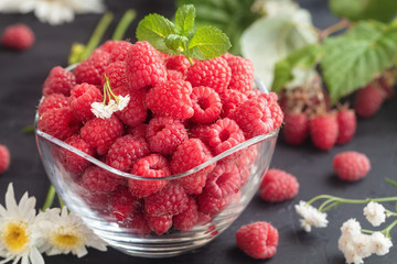Fresh Deluxe Raspberries in glass bowl with field flowers on dark wooden background. Close up, high resolution product. Harvest Concept - Image