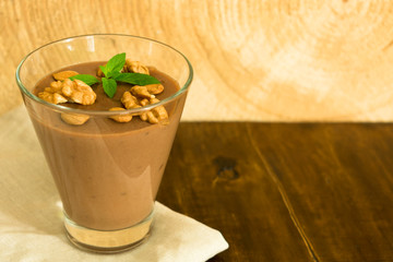 Dessert chocolate pudding with nuts in a glass on a wooden table. Copy space.	