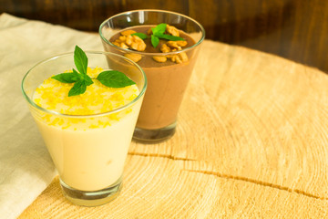 Dessert chocolate pudding with nuts and vanilla pudding with lemon zest on a wooden table.	