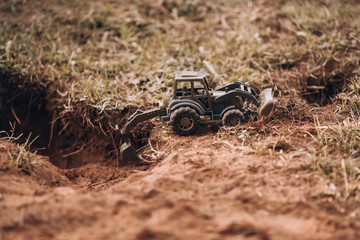 Tractor excavator works. A green tractor is digging a hole. Toy tractor in vintage color