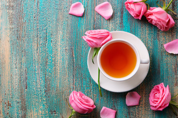 Fototapeta na wymiar Cup of tea with pink rose. Colorful turquoise wooden background. Top view. Copy space.