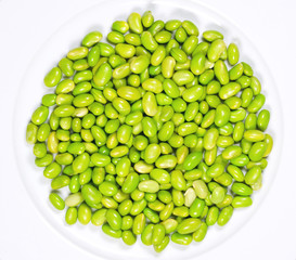 Edamame. Green soybeans on a white plate. Mukimame, unripe soya beans outside the pod. Glycine max, a legume, edible after cooking and a protein source. Closeup, on white background, macro food photo.