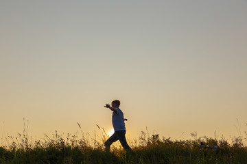 Black silhouette of cute happy kid happy to run alone in summer sunset meadow.
