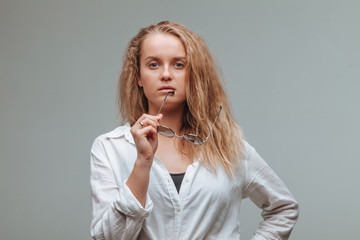 A girl in a white shirt nibbles glasses on a gray background