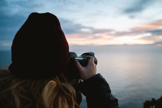 Photographer girl taking pictures during sunrise by the ocean