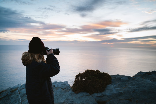 Photographer girl taking pictures during sunrise by the ocean