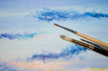 Artist paintbrushes closeup on artistic paintes canvas with evening clouds - painting, art and creativity concept