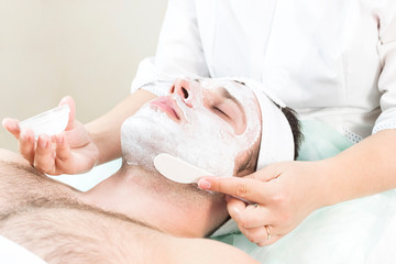 Obraz na płótnie Canvas Cosmetic procedure for applying a therapeutic mask to a young man in a beauty salon.