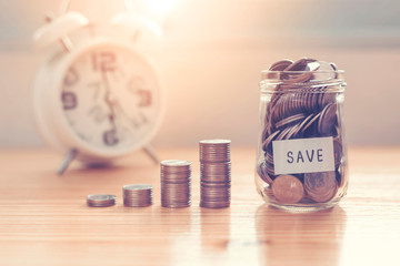 Coins in jar with money stack step growing on wood table in.money saving financial concept.retro vintage color tone.