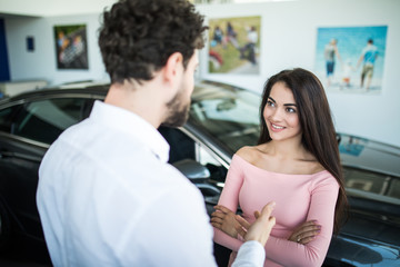 Successful young lady discussing her potential purchase with a car dealer in showroom