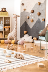 Stylish scandinavian newborn baby room with toys, children's armchair, teddy bear , soft toys and design furnitures. Modern interior decor with white background walls, wooden parquet. Template.