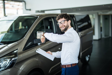 Fototapeta na wymiar Handsome car dealership worker smiling while standing near the car