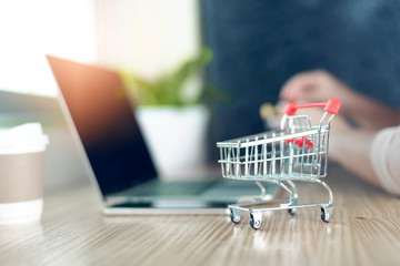 Red shopping cart on a laptop keyboard near the window at home.Easy shopping with finger tips for consumers.Online shopping concept.