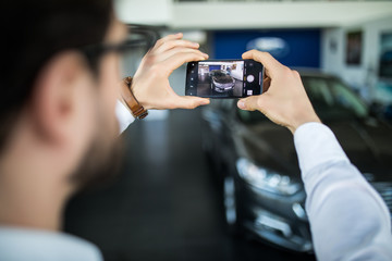 Visiting car dealership. Handsome man take photo with his new car