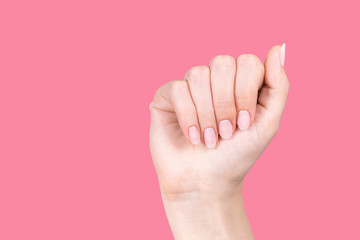 Closeup view of beautiful female hand with natural pink pastel manicure isolated on pink background. Horizontal color photography.