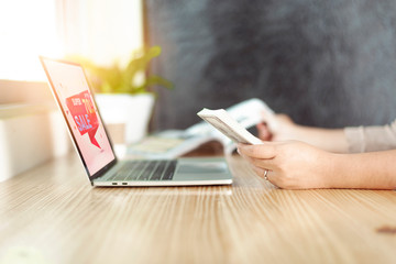 Asian woman holding dollar bills online shopping Website on Laptop on wood table near the window at home.Online shopping concept.