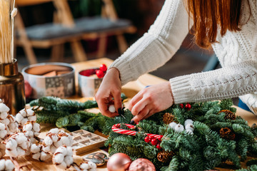 Festive interior design. Closeup of professional florist hands using green fir tree twig, cotton plant to create Christmas decor.