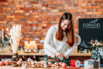 Florist workshop. Creative lady working on new festive winter decoration. Blur brick wall background. Copy space.