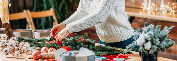 Craft workshop. Cropped shot of female florist using green fir tree twig to create Christmas interior decoration.