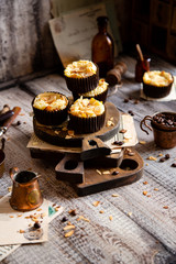 fresh baked homemade muffins with biscuit and cheesecake layers and almond petals on top stands wooden brown boards on grey table opposite concrete wall, selective focus