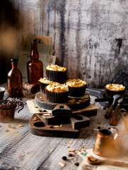fresh baked homemade muffins with biscuit and cheesecake layers and almond petals on top stands wooden brown boards on grey table opposite concrete wall, selective focus