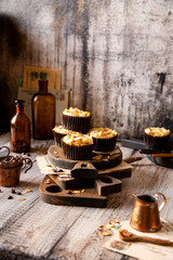 Fototapeta na wymiar fresh baked homemade muffins with biscuit and cheesecake layers and almond petals on top stands wooden brown boards on grey table opposite concrete wall, selective focus