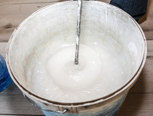 Man is mixing spackling glue in the bucket. Wallpaper hanging in the flat. Restoration indoors....