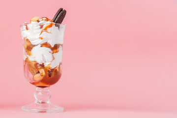 Sweet dessert in glass with biscuit and whipped cream on pink bsckground, selective focus and blank space