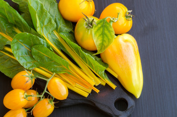 yellow vegetables, tomatoes pepper, chard on black background.