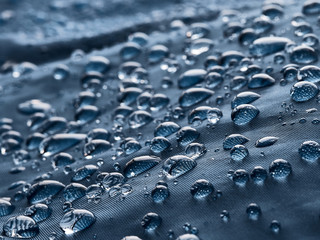 Rain water droplets on blue fiber waterproof fabric. Blue background.