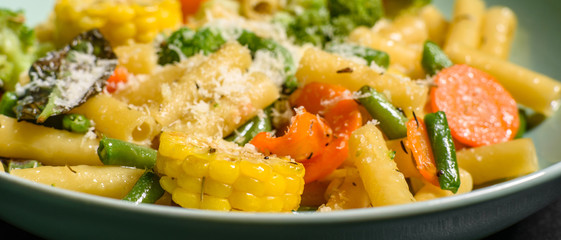 Delicious fresh warm paste sprinkled with cheese parmesan with broccoli, corn, carrots and other vegetables. Vegetarian food
