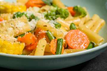 Delicious fresh warm paste sprinkled with cheese parmesan with broccoli, corn, carrots and other vegetables. Vegetarian food