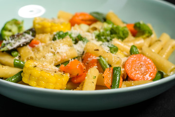 Delicious fresh warm paste sprinkled with cheese parmesan with broccoli, corn, carrots and other vegetables. Vegetarian food