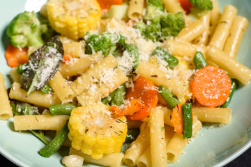 Delicious fresh warm paste sprinkled with cheese parmesan with broccoli, corn, carrots and other vegetables. Vegetarian food