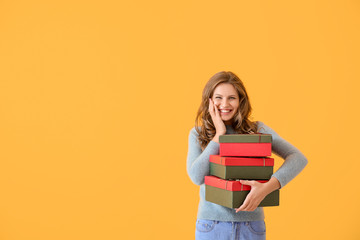 Happy young woman with Christmas gifts on color background