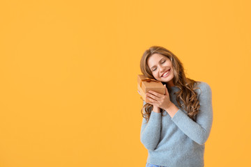 Happy young woman with Christmas gift on color background