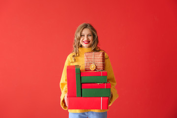 Happy young woman with Christmas gifts on color background