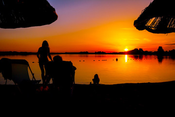 Obraz premium Silhouetted shot of sunset with people by the beach
