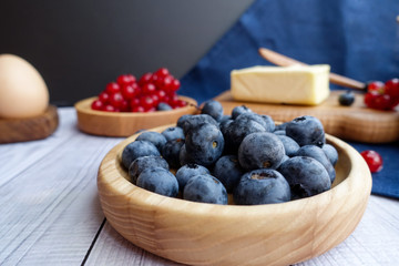 ingredients for baking lie on a light wooden background with a blue kitchen towel., butter, berries, a bun and wooden tools