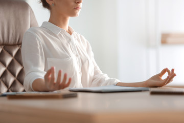 Young businesswoman meditating at workplace in office