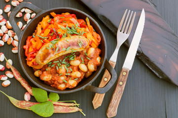 Stewed beans with vegetables and sausages. on black background.