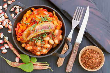 Stewed beans with vegetables and sausages. on black background.