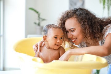 Young African-American mother washing her baby at home